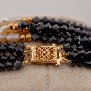 Black beaded necklace with gold clasp on a textured surface