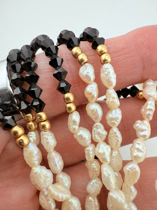 Three-strand pearl necklace with black, gold, and white beads on a hand against a white background.