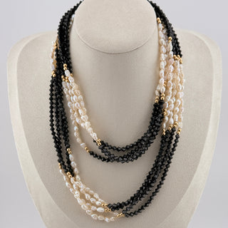Necklace with black, white, and gold beads on a white stand against a light gray background