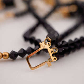 Gold clasp on a black beaded necklace with blurred background