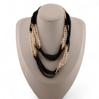 Necklace with black, white, and gold beads on a white stand against a light gray background