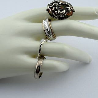 A set of four silver rings displayed on a white mannequin hand. The rings include a textured filigree ring with a small amber stone, a chevron-patterned band, a simple smooth band, and a twisted band.