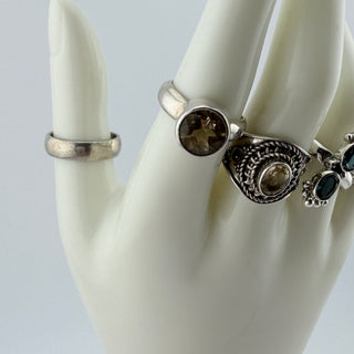 Three silver rings with smoky brown and dark green gemstones displayed on a white ceramic mannequin hand against a light gray background.