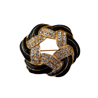 Black and gold brooch with crystal detailing on a light gray background