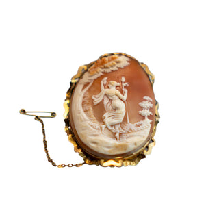 Antique carved cameo brooch pin in gold frame depicting a shapely woman holding a staff and looking over her shoulder, with a safety chain.