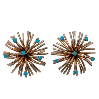 A pair of gold-tone metal clip-on earrings with a starburst design and blue rhinestone accents.