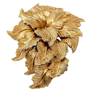 A vintage gold-colored metal brooch in a gold leaf design, featuring a textured surface and pin clasp.