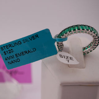 A sterling silver nano band ring with green emerald-cut stones, displayed on a white jewelry stand with a blue price tag and size tag attached.