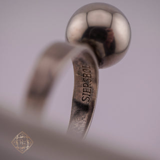 A close-up of a silver ball ring with a polished metallic finish and a band engraved with 'SIERSBOE'.