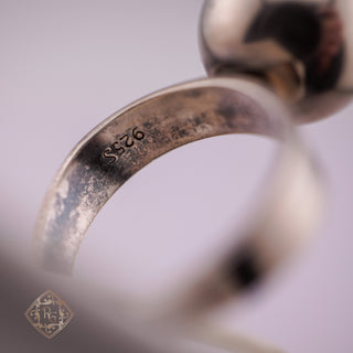 Close-up of a sterling silver ring band with '925' silver purity stamp, showing a textured, oxidized finish against a soft lavender background.