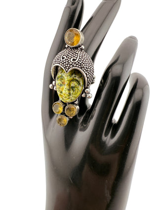 Decorative ring with green and yellow gemstones on a black hand model
