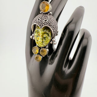 Silver ring with yellow gemstones on a black mannequin hand against a white background