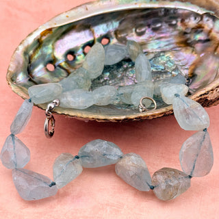 Transparent gemstone necklace on a pink background with an abalone shell