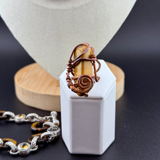 Jewelry display with a copper ring, necklace, and bracelet on a white stand.