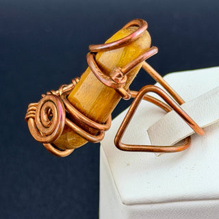 Decorative ring with Tiger's Eye and copper wire on a white surface with dark background