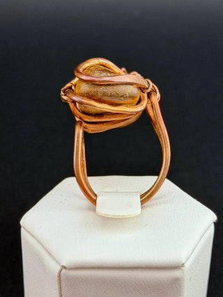 Gold ring with a central stone on a white stand against a black background