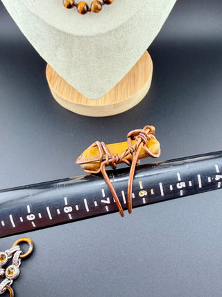 Jewelry with a stone and brown cord on a black surface with a ruler.
