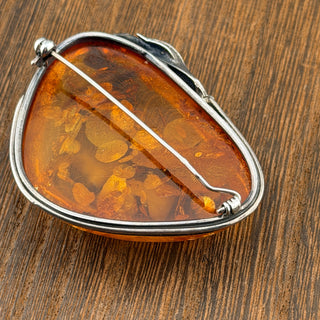 Amber brooch with silver setting on a wooden surface