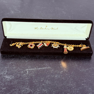 Gold charm bracelet with various charms in a 'The Berkeley Mint' box on a dark surface.