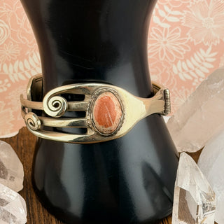 Gold bracelet with a red stone on a black mannequin against a floral background