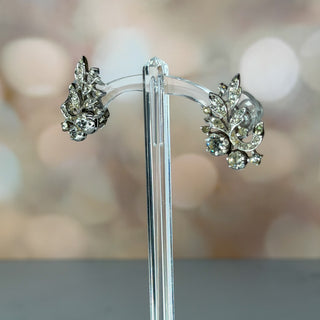Pair of silver earrings on a clear stand with a blurred background