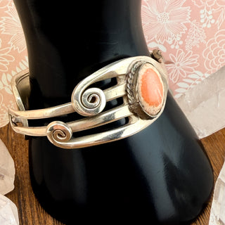 Silver bracelet with a coral stone on a black vase with a floral background