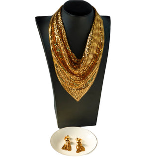 A vintage gold mesh necklace displayed on a mannequin bust and a pair of matching tassel dangle drop clip earrings on a white plate, both appear yellow metal.