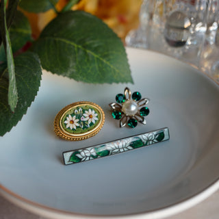 Three pieces of jewelry on a white plate with green leaves in the background