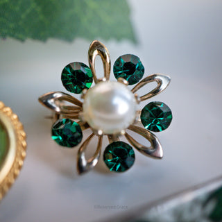 Gold brooch with a pearl and green gemstones on a light background