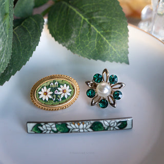 Three decorative pins on a white surface with green leaves in the background