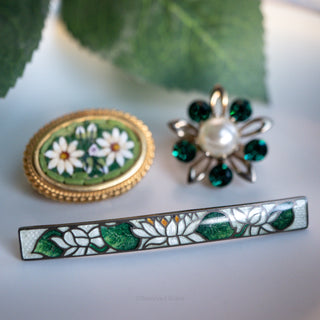 Three decorative brooches with floral designs on a light background.