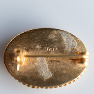 Gold brooch with 'ITALY' engraving on a light gray background
