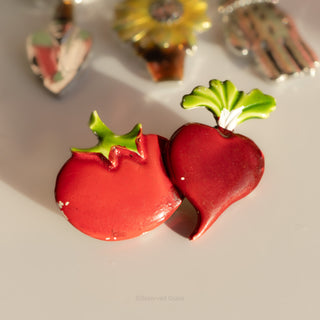 Red apple-shaped earrings with green leaves on a reflective surface.