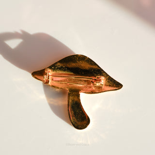 Gold leaf-shaped object on a white surface with a soft shadow