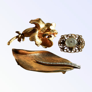 Three gold brooches on a light purple background