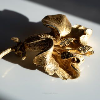 Gold floral brooch with embedded stones on a reflective surface