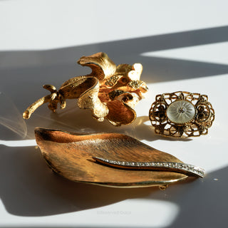 Three gold brooches on a white surface with shadows