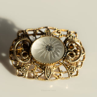 Decorative gold brooch with intricate design on a light background