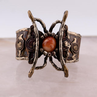 Reserved Grace handmade Brutalist cuff bracelet with a textured metal butterfly wing frame and orange glass cabochon.