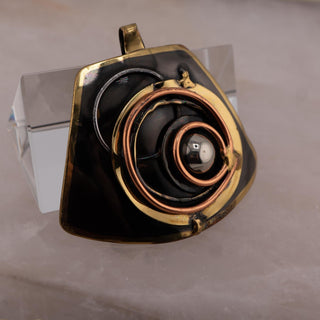 Reserved Grace brutalist pendant featuring layered bronze and copper spiral details on a dark mixed metal base.