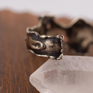 Reserved Grace artisan brutalist cuff bracelet in silver tone metal with textured edges resting on a quartz crystal.