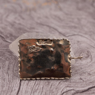 Reserved Grace hand-stamped rectangular silver pendant with a twisted border and artist signature on a wooden surface.