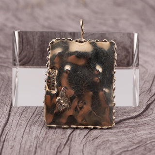 Reserved Grace hand-stamped rectangular silver pendant with a twisted edge and signature detail on a wooden surface.