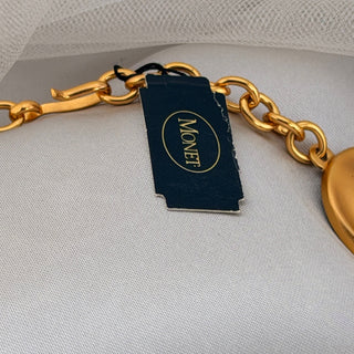 Reserved Grace vintage Monet gold-tone necklace featuring a matte disk design and signature brand tag on a white cloth.