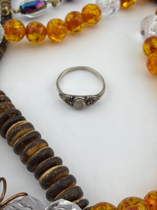 Reserved Grace sterling silver ring surrounded by amber beads and dark wood discs on a white background