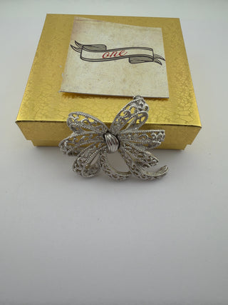 Reserved Grace vintage Trifari silver-tone filigree bow brooch with intricate lacy loops on a gold gift box