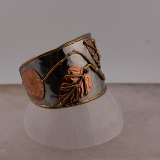 Reserved Grace Anju tri-tone cuff bracelet featuring silver, copper, and brass leaf appliqués on a wide metal band.