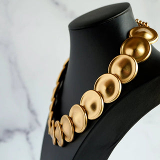 Reserved Grace vintage gold-tone necklace featuring a sequence of matte circular disks on a black display bust.