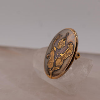 Reserved Grace vintage 1985 Norwegian hand-painted ceramic brooch with abstract gold luster glaze on a grey background.