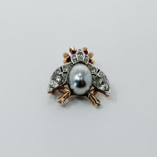Reserved Grace vintage Trifari insect brooch with a silver-gray cabochon body, clear rhinestones, and red accents.